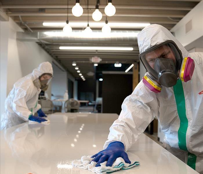 Servpro crew disinfecting counter in full PPE